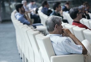 Starszy Pan w fotelu konferencyjnym, pośród innych uczestników konferencji