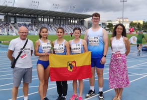 Sportowcy z opiekunami i flagą Leszna